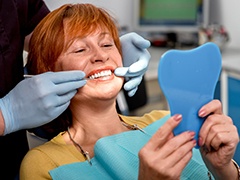 Senior woman in dental chair looking at smile in mirror
