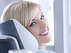 A young woman sitting in the dentist’s chair and smiling after receiving her dental implants