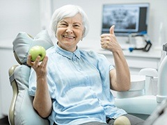 elderly woman giving a thumbs up and holding a green-yellow apple