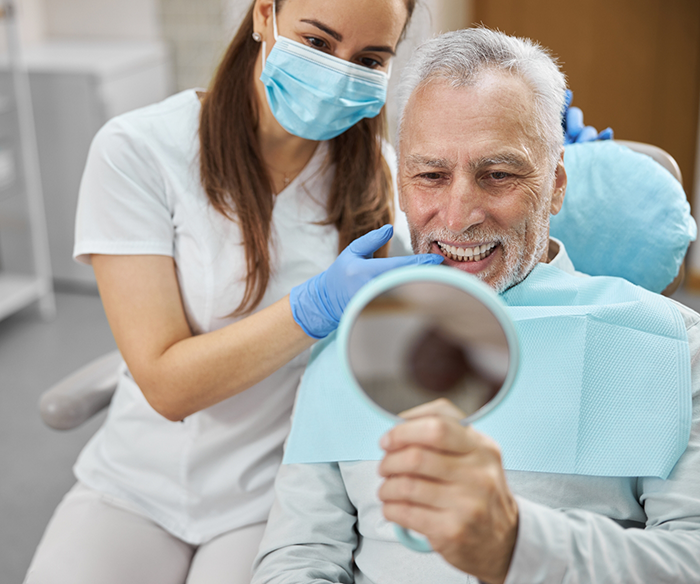 Senior man admiring his new smile in a mirror with All on 4 dental implants in Torrance