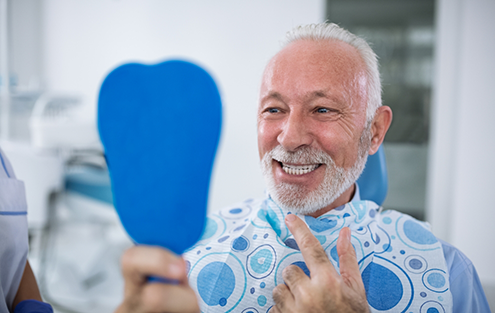 Senior man in dental chair looking at his smile in a mirror