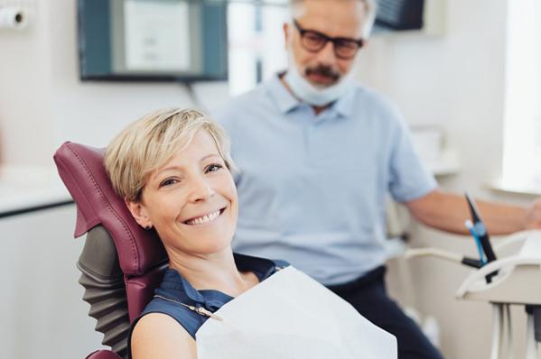 woman in dental chair, smiling, with dentist in background