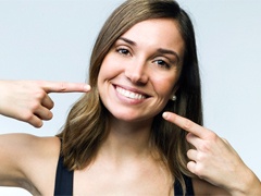 A young woman with dark hair pointing to her smile after cosmetic dentistry