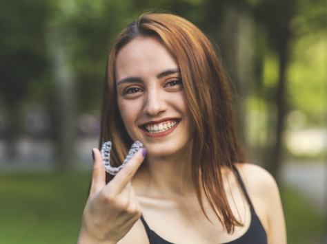 Smiling woman holding an Invisalign clear aligner