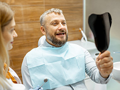 a patient looking at their dental crown in a handheld mirror