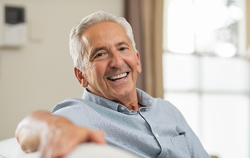 Smiling man sitting on couch with his arm draped over the back of it