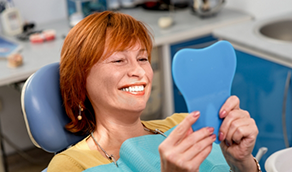 Redheaded woman in dental chair looking at her smile in a mirror