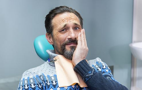 Man in dental chair wincing in pain while holding his face