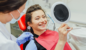 Young woman in dental chair looking at her smile in a mirror