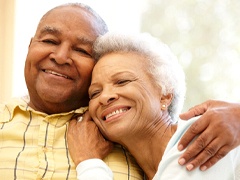 An older couple hugging and smiling while seated on a couch