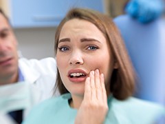 Woman with broken dental crown in dental chair holding cheek