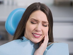 Woman in dental chair holding face in pain before emergency dentistry