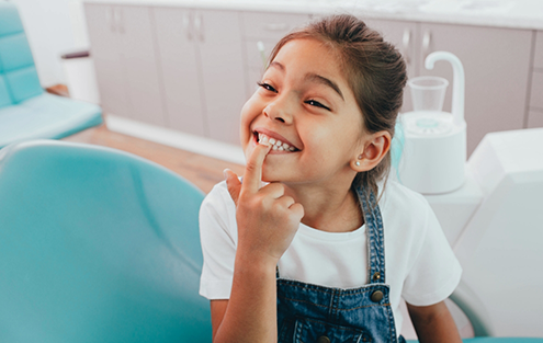 Young girl in dental chair pointing to her teeth