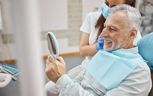 Senior man in dental chair looking at his smile in a mirror