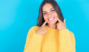 Woman in yellow sweater pointing to her smile