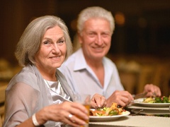 An older couple seated at a table and eating a healthy dinner with the help of their dental implants