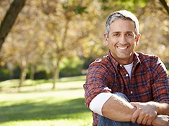 A middle-aged man sitting outside on the grass and smiling after learning proper dental implant care in Torrance