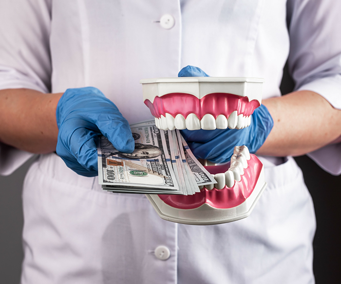 Dentist holding a model of the teeth that is holding hundred dollar bills