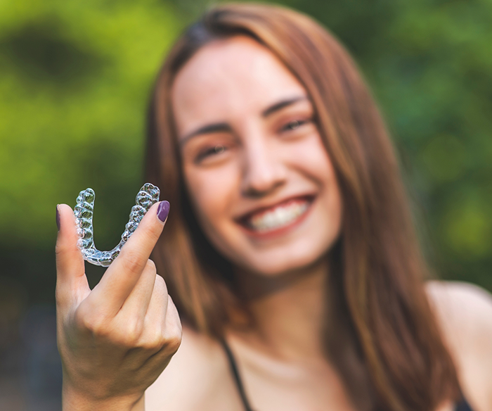 Smiling woman holding an Invisalign clear aligner in Torrance