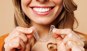 Smiling woman holding an Invisalign tray near her mouth