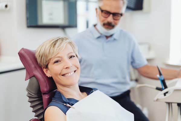 woman in dental chair, smiling, with dentist in background