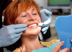 Senior woman in dental chair looking at smile in mirror