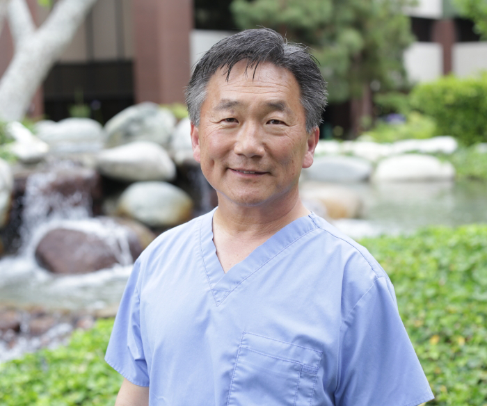 Torrance prosthodontist Doctor George Cho smiling in front of a small waterfall