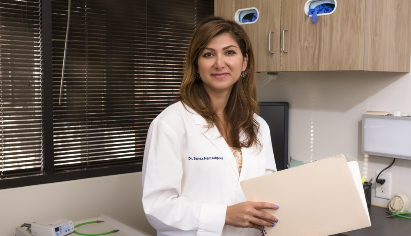 Doctor Hamzehpour wearing a white lab coat and holding a manila folder