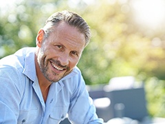 Man in light blue shirt sitting outside and smiling