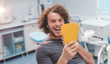 Young man admiring his smile in a mirror after dental services in Torrance