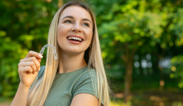 Smiling woman holding an Invisalign clear aligner