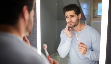 Man holding his toothbrush and wincing in pain