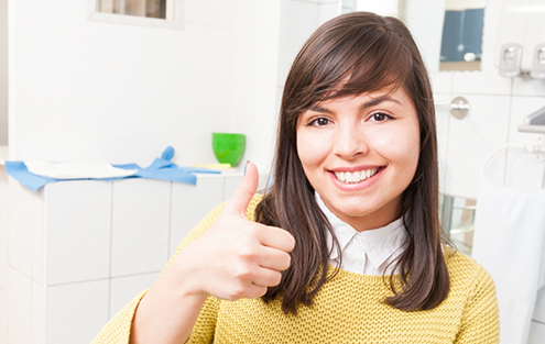Woman in yellow sweater giving a thumbs up in dental chair
