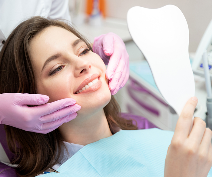 Dental patient admiring her teeth in a mirror after a smile makeover in Torrance