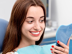 Woman looking at smile in mirror after teeth whitening