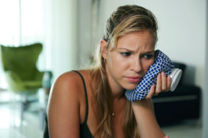 Young woman with toothache holding ice bag on cheek