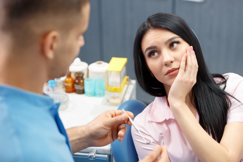 A woman holding her mouth in pain at the dental office.