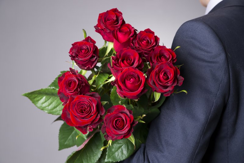 man black suit holding a dozen roses