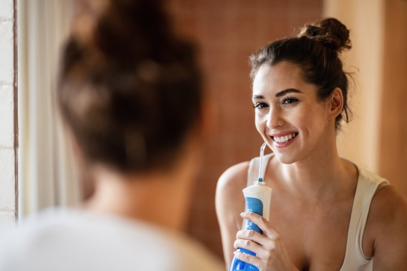 a young woman standing in the mirror and using a water flosser