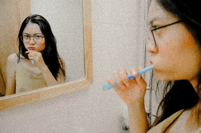 Woman brushing her teeth in front of the bathroom mirror.