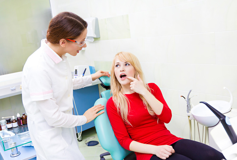 Patient needing a dental filling pointing to mouth at dentist